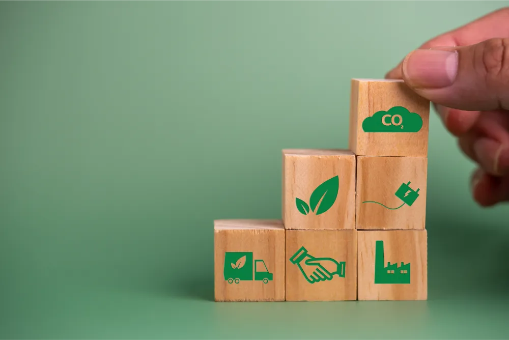 Holzwürfel mit grünen ökologischen und energetischen Symbolen vor grünem Hintergrund von oben von einer Hand gehalten